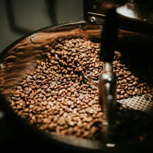 Close-up of freshly roasted coffee beans in a large industrial coffee roaster, showcasing rich textures and warm tones.